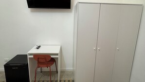 A room with a flat-screen TV mounted on the wall, a white desk with a chair, and a wardrobe. - Caltur B&B (Palermo)