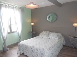A bedroom with a bed, two bedside tables, a round mirror, and a window with curtains.