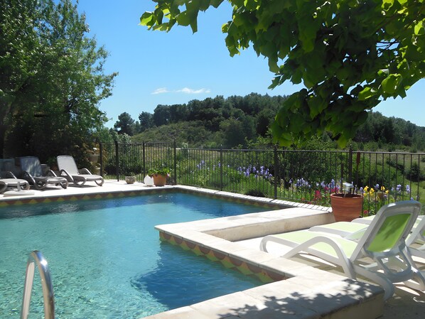 A clear swimming pool with lounge chairs and potted plants around it.