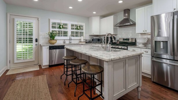 A modern kitchen with white cabinets, stainless steel appliances, and a large island with stools.