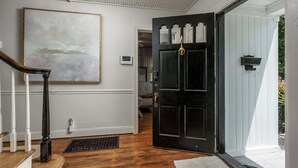 A hallway with a wooden staircase, a black door, a white wall, and a painting.