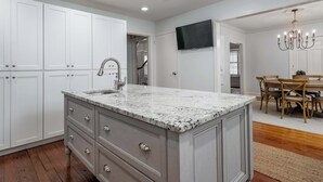 A kitchen with white cabinets, a granite countertop, and a dining area with wooden chairs and a table.