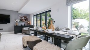 Ein moderner Essbereich mit großem Fenster, einem flachbildschirmfernseher an der Wand und einem Esstisch, gedeckt mit Tellern, Gläsern und einer Vase.
