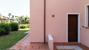 A pink building with a wooden door, a small white bench, and a tiled pathway leading to the entrance. - Terrazza al Poggio by Wonderful Italy (Porto Rotondo)