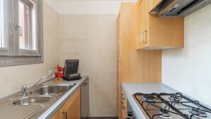 A compact kitchen with a gas stove, stainless steel sink, and wooden cabinets. - Terrazza al Poggio by Wonderful Italy (Porto Rotondo)