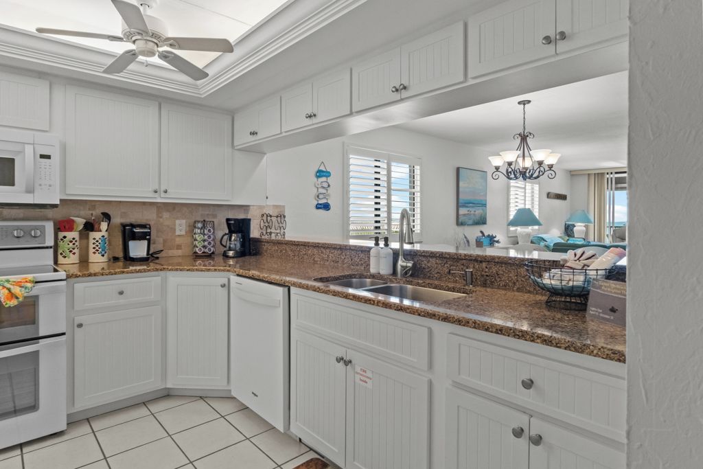 A modern kitchen with white cabinetry, granite countertops, a built-in oven, and a ceiling fan.
