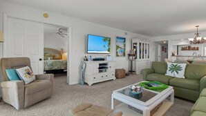 A living room with a sofa, armchair, and ottoman, a coffee table, a TV, and a cabinet with decorative items. - Beautiful panoramic views of the Gulf, 2 bedroom w/sleeping den, 2 bath condo (Sanibel)