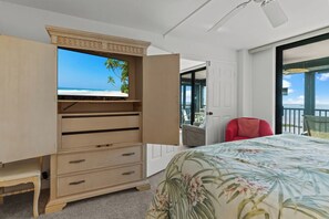 A bedroom with a bed, a wooden dresser, a red chair, and a balcony with a view of the ocean.