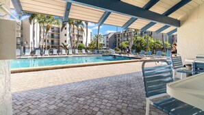 A pool area with lounge chairs and umbrellas, surrounded by buildings and palm trees. - Beautiful panoramic views of the Gulf, 2 bedroom w/sleeping den, 2 bath condo (Sanibel)