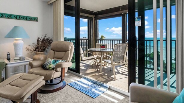A balcony with a view of the ocean, a round table with chairs, a beige armchair, a small table with a lamp, and a map on the floor. - Beautiful panoramic views of the Gulf, 2 bedroom w/sleeping den, 2 bath condo (Sanibel)