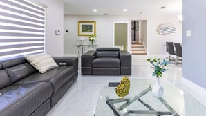 Uma sala de estar moderna com um sofá de couro, uma mesa de centro de vidro e uma área de refeições com cadeiras.
