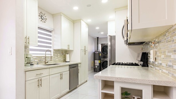 Uma cozinha moderna com armários brancos, lava-louças de aço inoxidável, forno embutido e painel de azulejos.