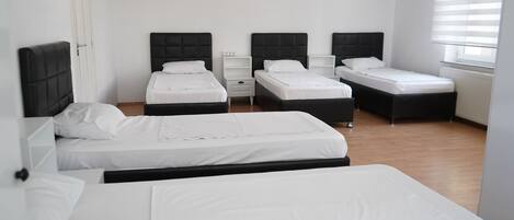 A hotel room with three beds, white bedding, and black headboards.