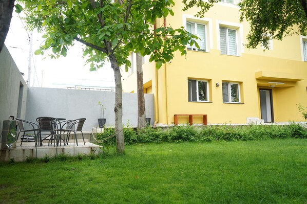 A yellow building with a small garden area, a tree, and outdoor furniture.