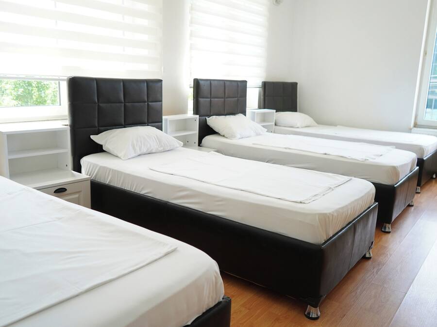 A hotel room with three beds, white bedding, and a window with blinds.