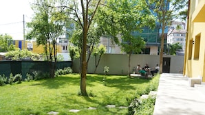 A courtyard with a grassy area, a tree, and a seating area with people. - HOTEL GREEN GARDEN (Bucharest)