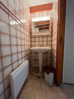 Un bagno compatto con un lavandino bianco, uno specchio sopra e un termosifone a sinistra.