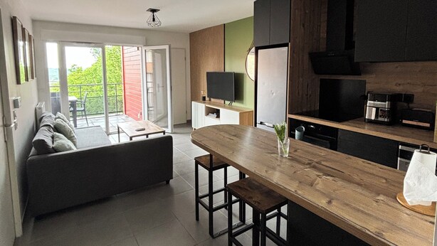 A modern kitchen with a wooden island, black cabinets, and a large window overlooking a garden. - Bright apartment 15 minutes from Bayonne (Lahonce)
