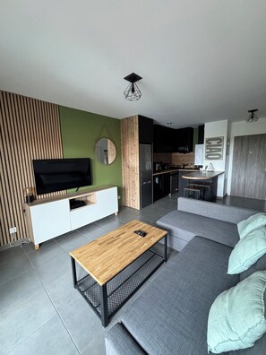 A modern living room with a grey sofa, a wooden coffee table, and a television on a white cabinet. - Bright apartment 15 minutes from Bayonne (Lahonce)