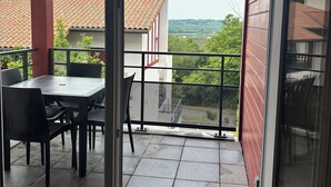 A balcony with a table and chairs, a red wall, and a view of buildings and trees. - Bright apartment 15 minutes from Bayonne (Lahonce)
