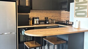 A modern kitchen with dark cabinetry, a wooden countertop, and a built-in island with stools. - Bright apartment 15 minutes from Bayonne (Lahonce)