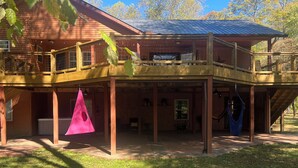 A two-story wooden house with a balcony, a hot tub, and a hammock.
