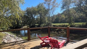 A wooden deck with red chairs overlooking a pond, surrounded by trees and a wooden railing.