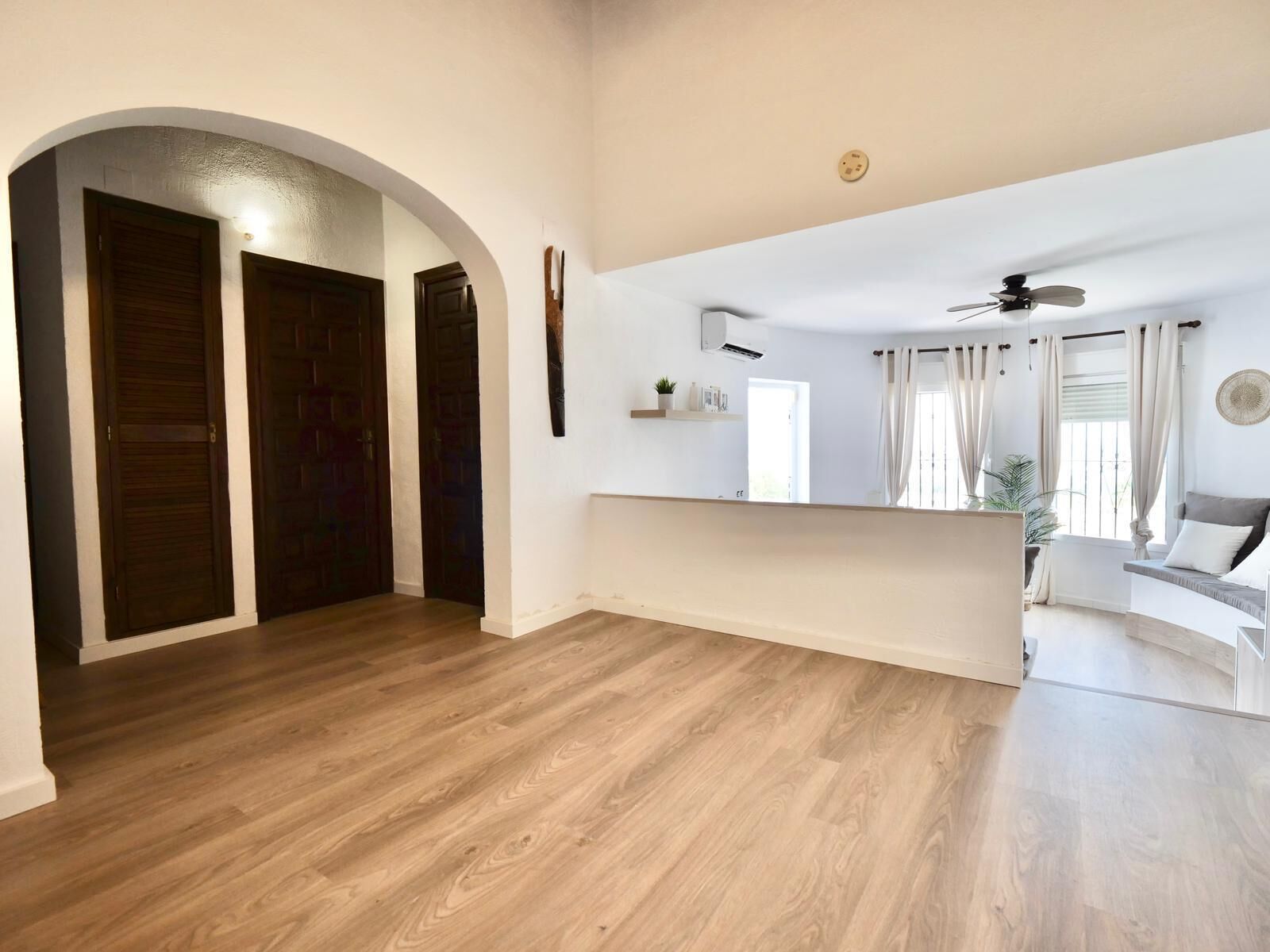 A spacious living area with wooden flooring, a ceiling fan, and a seating area with a sofa and curtains.
