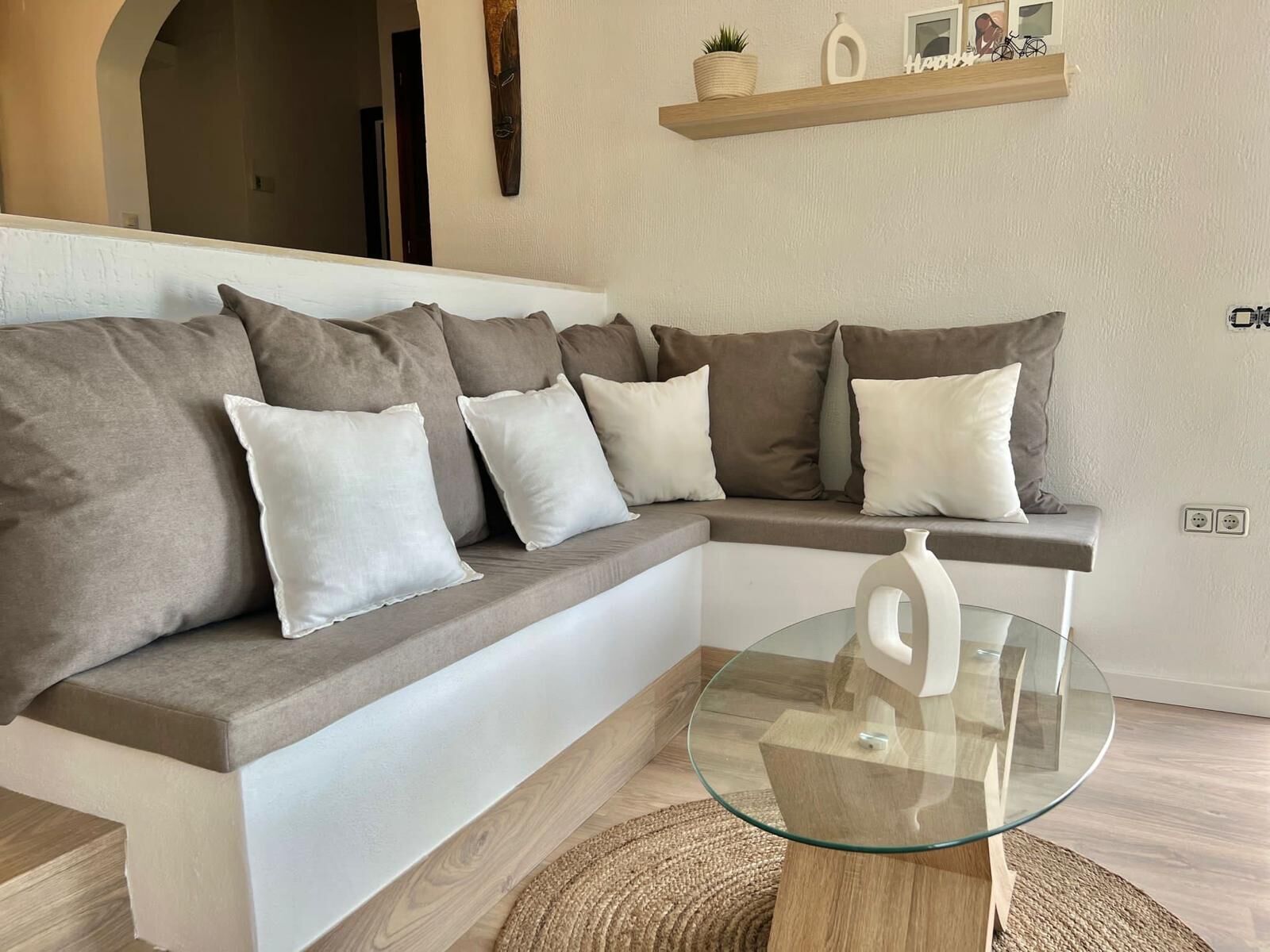 Uma sala de estar moderna com um sofá modular cinza, uma mesa de centro de vidro e piso de madeira.