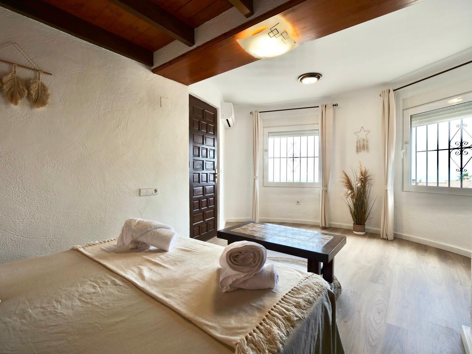 A room with a bed, a small table, a window with bars, and a ceiling light.