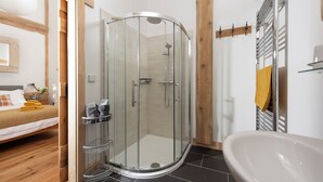 Een moderne badkamer met een douchecabine, een vrijstaand bad en een houten bed met nachtkastje.