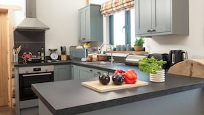 Een moderne keuken met grijze kastjes, een roestvrijstalen afzuigkap, een houten aanrechtblad en een raam met een ruitjes gordijn.