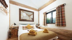 Een opgemaakt bed met een bruin dekbed, een bedlampje en een houten nachtkastje.