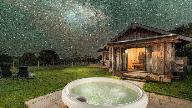 Een houten hut met een jacuzzi in een achtertuin, onder een sterrenhemel.