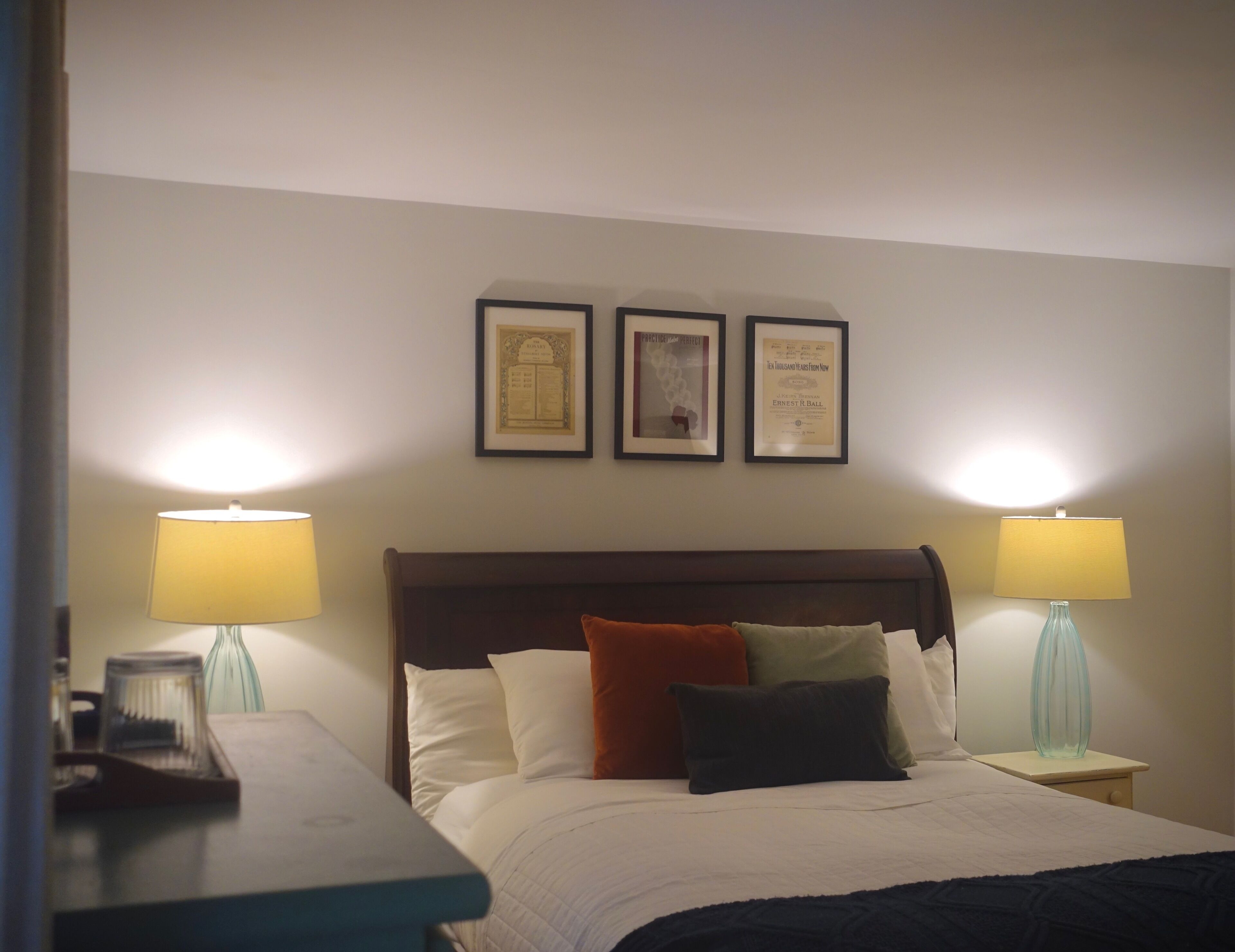 Una habitación de hotel con una cama, dos lámparas de noche y tres certificados enmarcados en la pared.