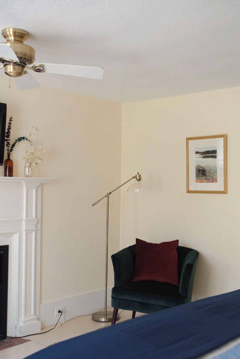 A room with a fireplace, a floor lamp, a framed picture on the wall, and a green chair with a red pillow.