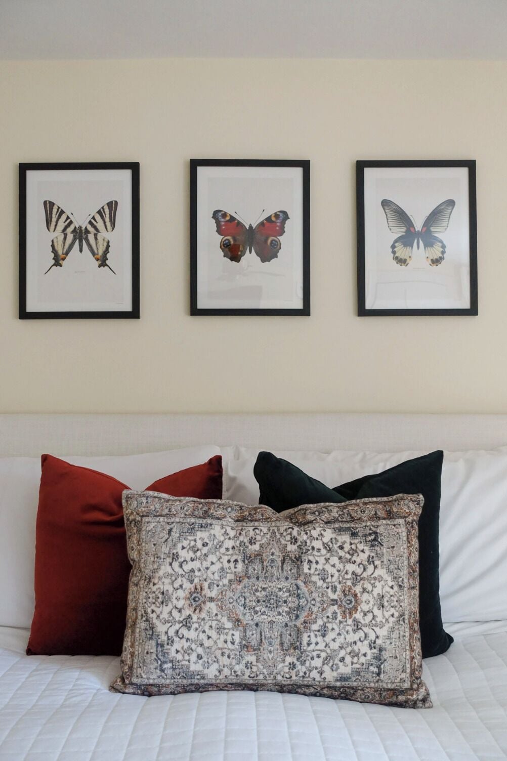 Una cama con tres almohadas y tres cuadros con mariposas en la pared.