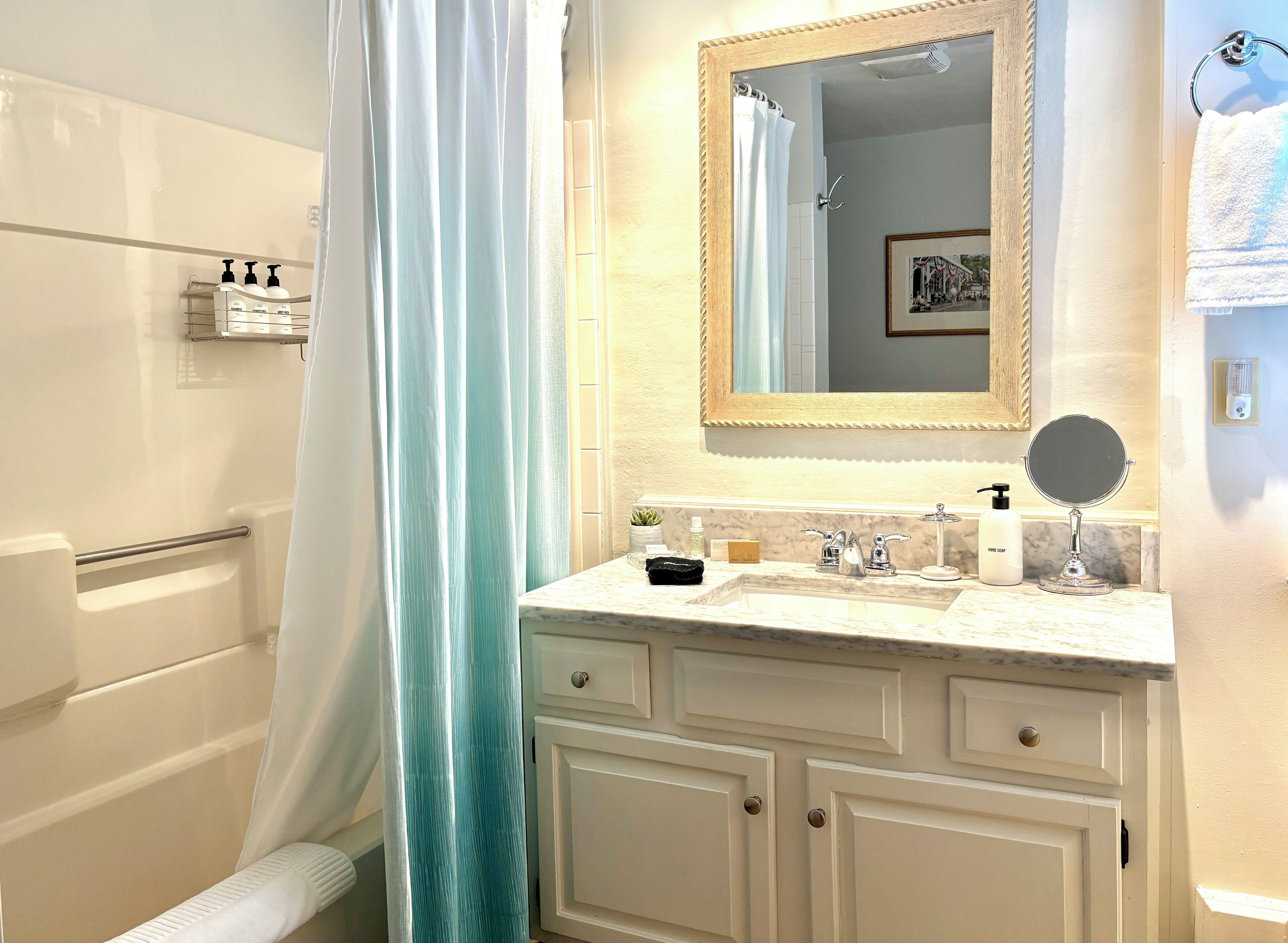 Une salle de bain avec une baignoire, un rideau de douche, un meuble-lavabo avec un miroir et des articles de toilette.