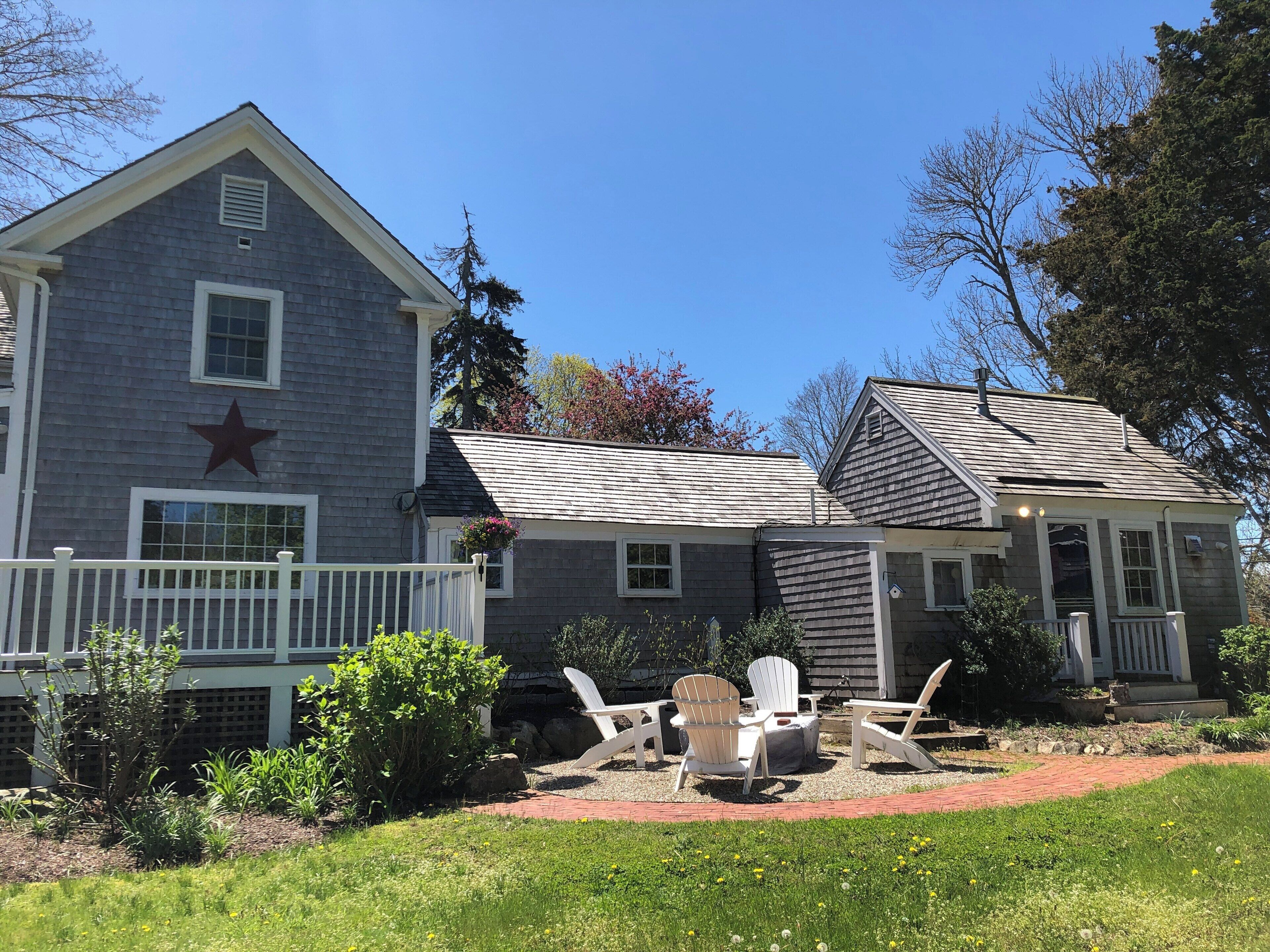 A two-story house with a star on the side, a porch with Adirondack chairs, and a garden area.
