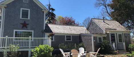 A two-story house with a star on the side, a porch with Adirondack chairs, and a garden area.