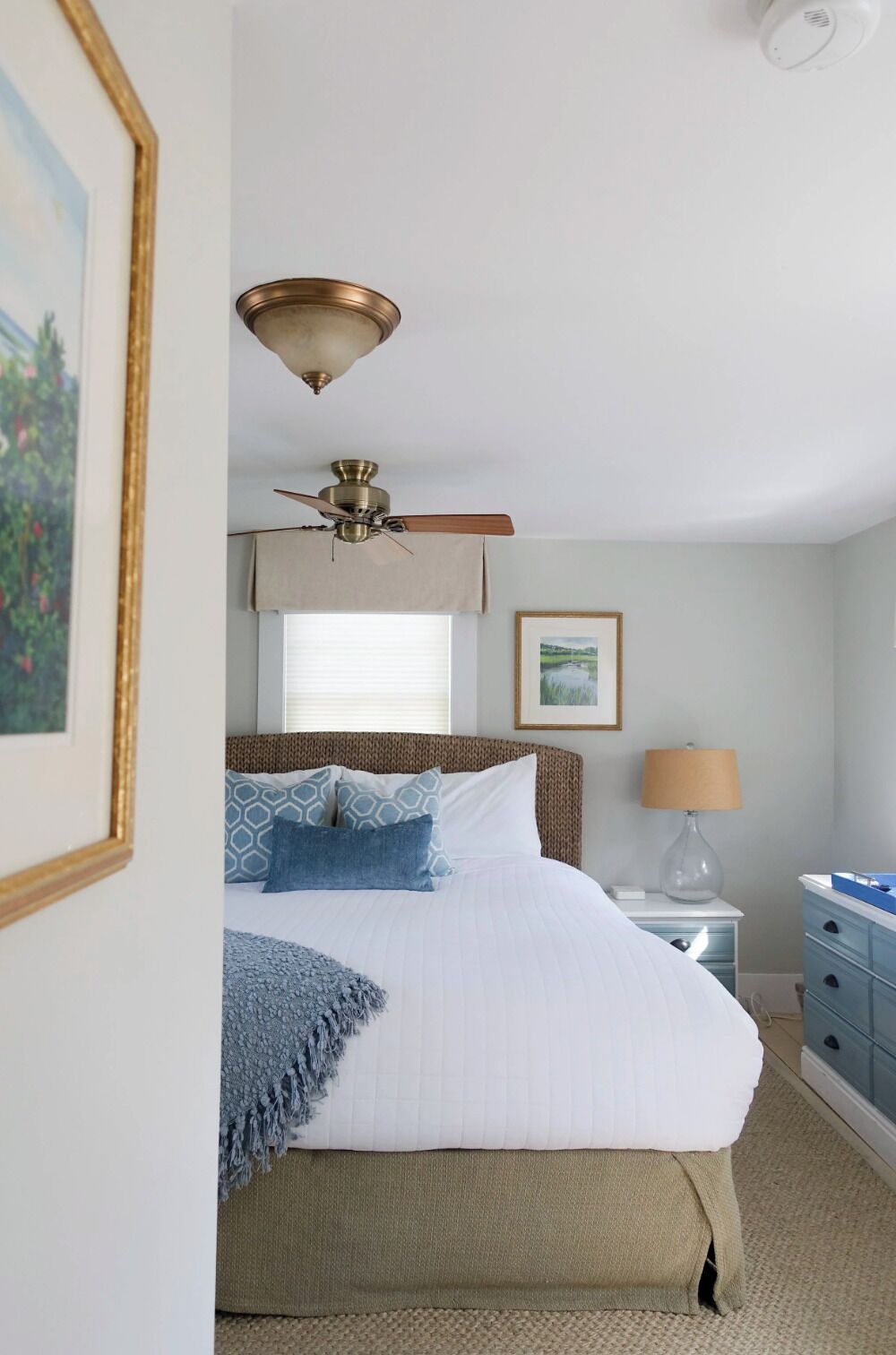 A bedroom with a bed, a ceiling fan, a bedside table with a lamp, and a dresser.