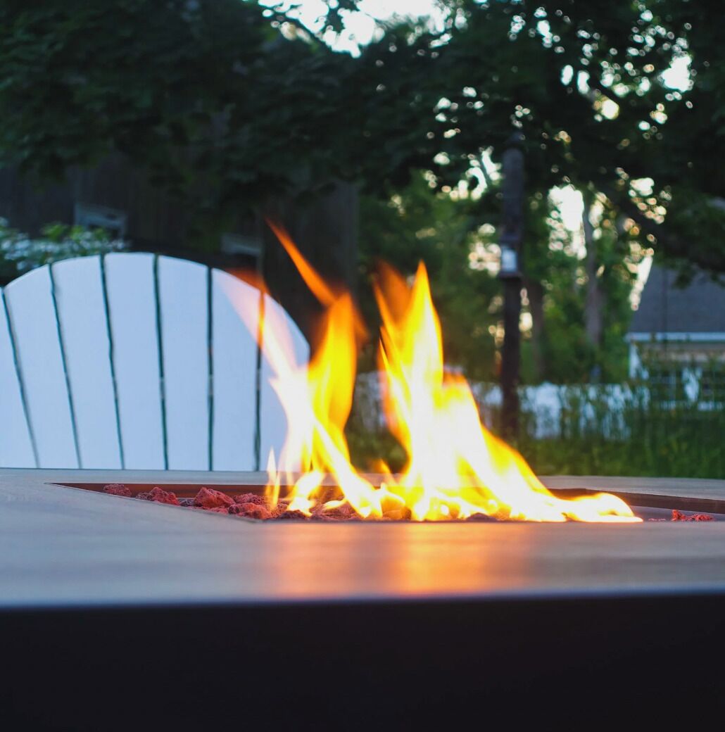 A fire feature with flames, a white chair, and a paved surface.