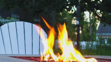 A fire feature with flames, a white chair, and a paved surface.