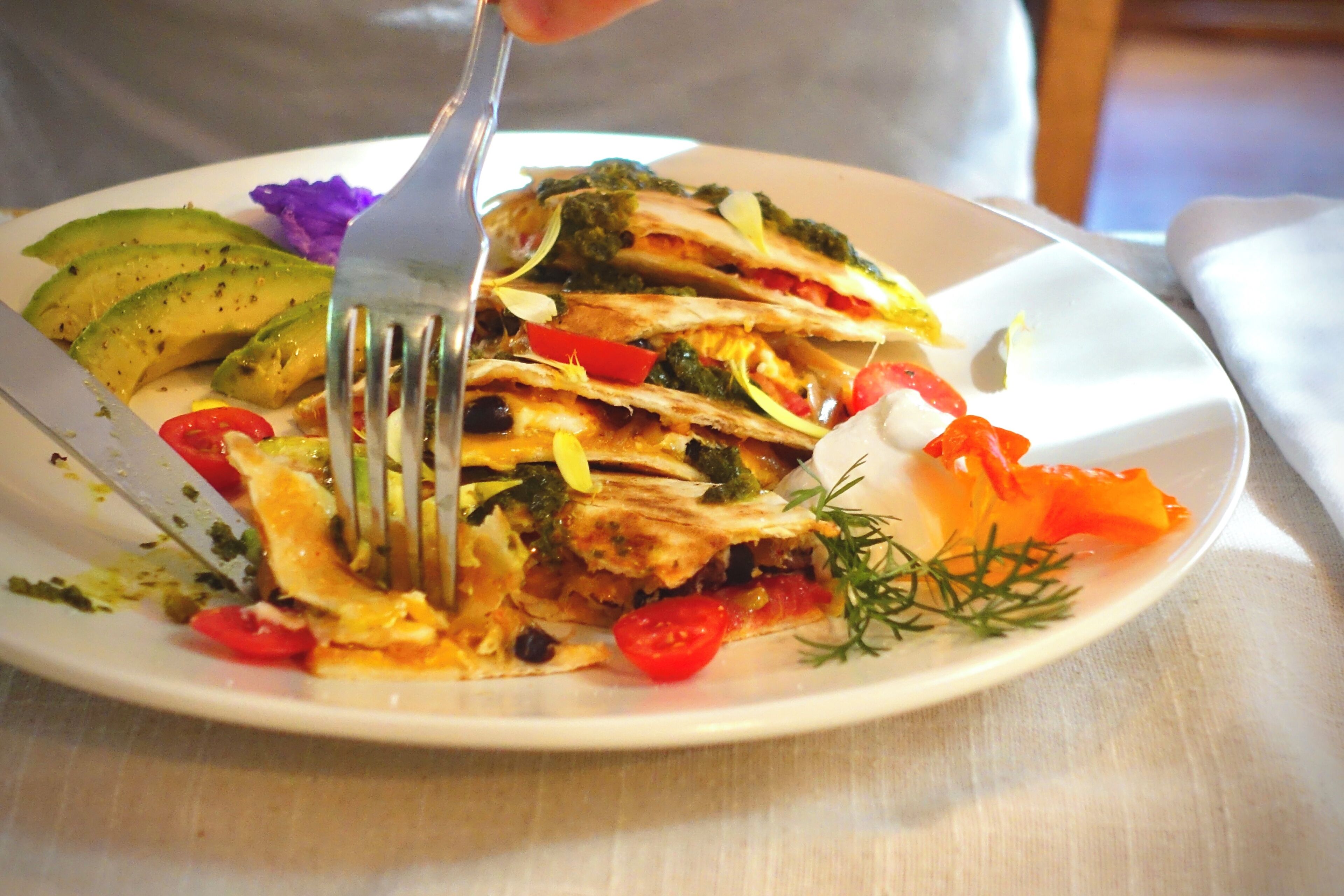 A plate with a quesadilla, avocado slices, and a fork.
