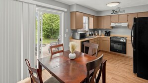 A modern kitchen with wooden cabinets, a black refrigerator, a microwave, a stove, and a coffee maker. - Near Razorback Stadium & Attractions, Firepit (Springdale)