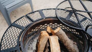 A fire pit with logs, surrounded by metal chairs and a bench.