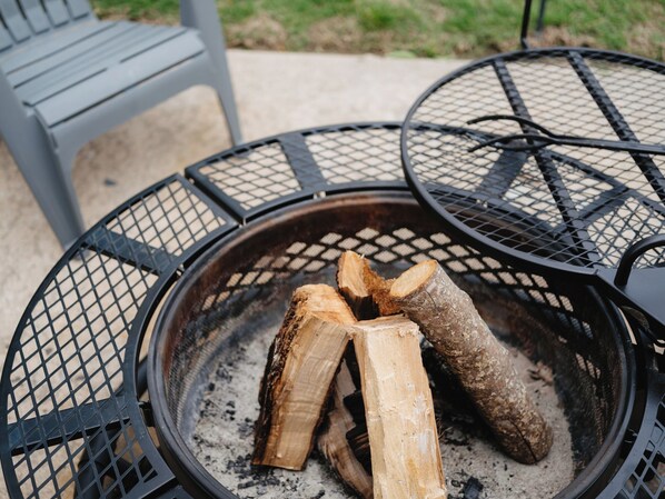 A fire pit with logs, surrounded by metal chairs and a bench.