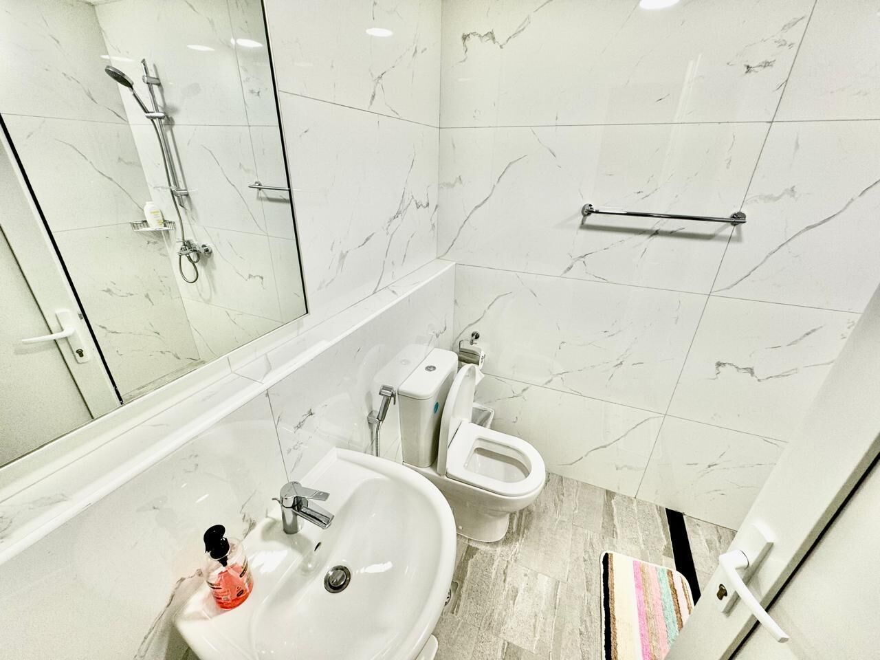 A modern bathroom with a marble floor, a white sink, a toilet, and a shower area.