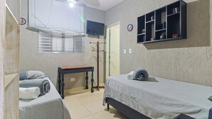 Un dormitorio con dos camas individuales, una mesa de madera, un televisor montado en la pared y un estante con objetos decorativos.
