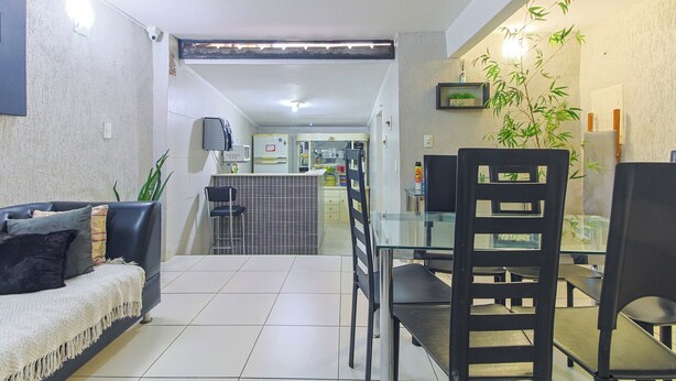 Una sala de estar moderna con un sofá, una mesa de comedor con sillas, una cocina al fondo y una planta de bambú en la pared.